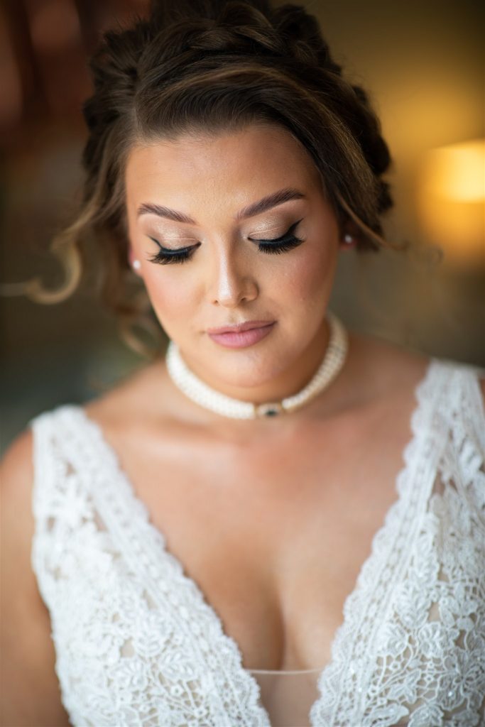 Bride looking down to show her eyelashes. She is wearing a white dress and a pearl necklace.