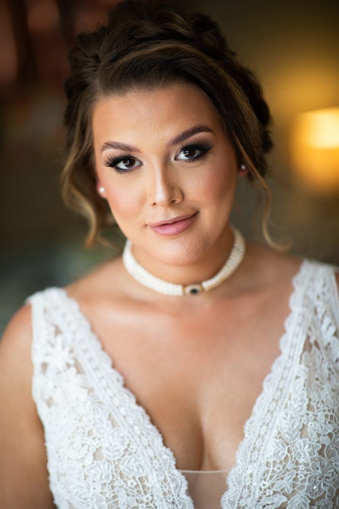 Bride smiling showing her eyelashes and lipstick. She is wearing a white dress and a pearl necklace.