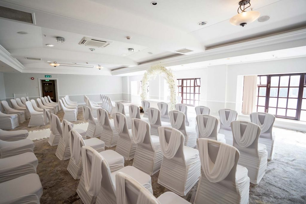 Photo of Aylesford Suite set up for a wedding ceremony with round tables and white chair covers
