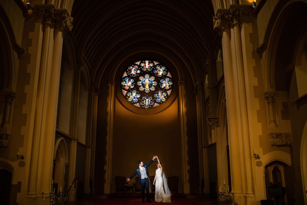 Bride and groom dancing in Stanbrook Abbey with the sun shining through the stained glass window