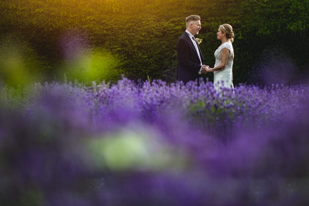 Bride ands Groom standing in a lavender garden looking at each other. 